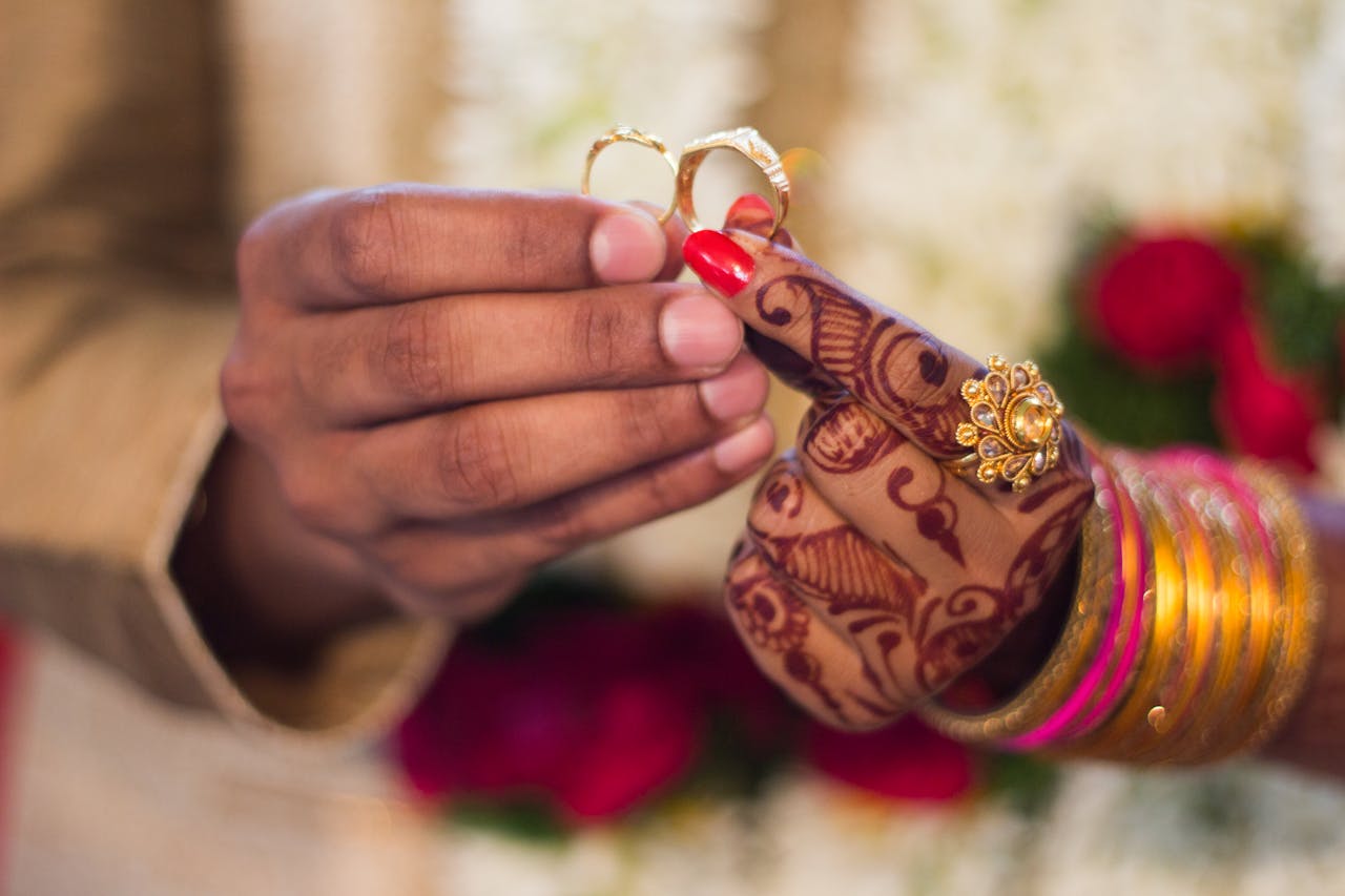 Home Close-up of hands with henna and jewelry during a traditional Indian wedding ceremony, exchanging rings.