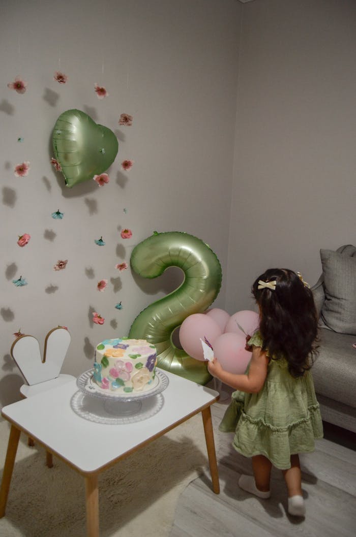 Home A little girl in a green dress celebrates her second birthday with decorations and cake.